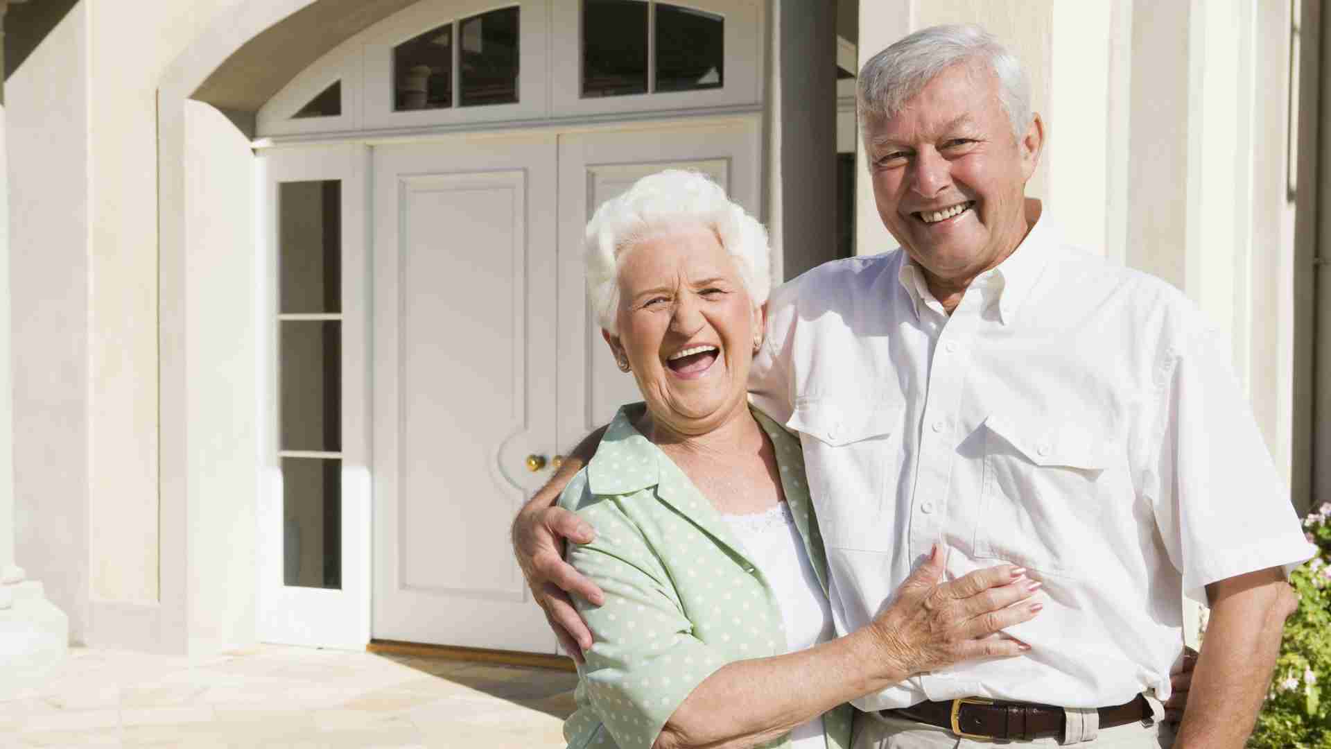 Elderly couple standing outside their house learning why it's good to put a house in a trust